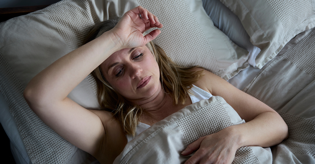 Sichtlich erschöpfte Frau liegt im Bett und greift sich an den Kopf.  © Shutterstock