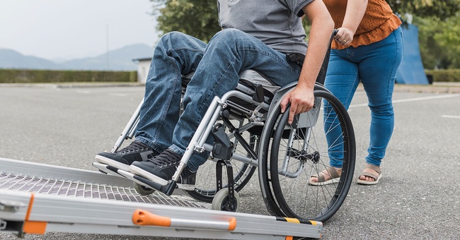 Mann in Rollstuhl wird von Pflegerin geschoben © Shutterstock